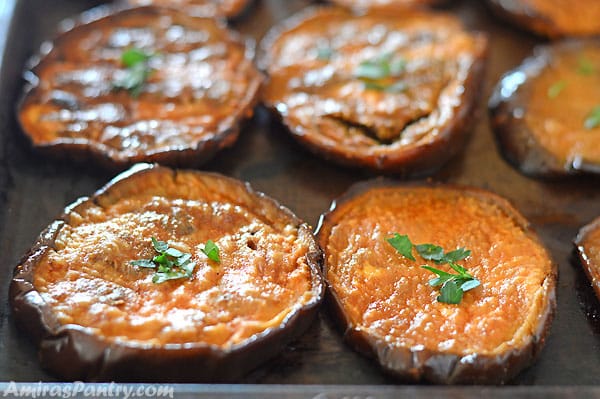 Oven roasted eggplant slices on a baking sheet and garnished with parsley.