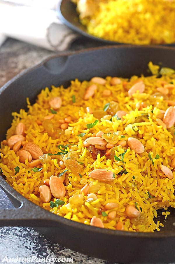 Yellow rice in a cast iron pan garnished with nuts and parsley.