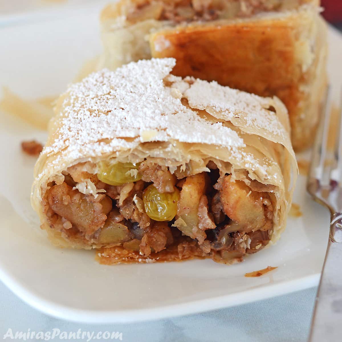 An apple strudel piece on a white plate with a fork next to it