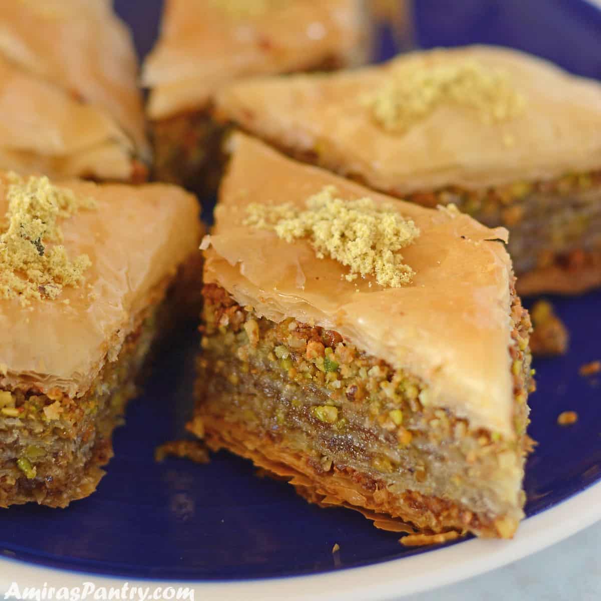 Baklava pieces placed on a blue plate and garnished with crushed pistachios.