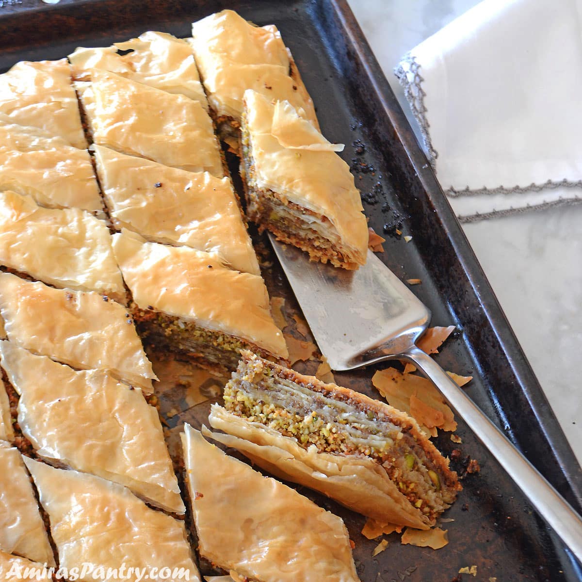 A dark baking sheet with baklava squares and one turned on its side to show the layers.