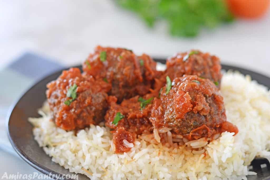 meatballs with tomato sauce over a bed of rice on a black plate.