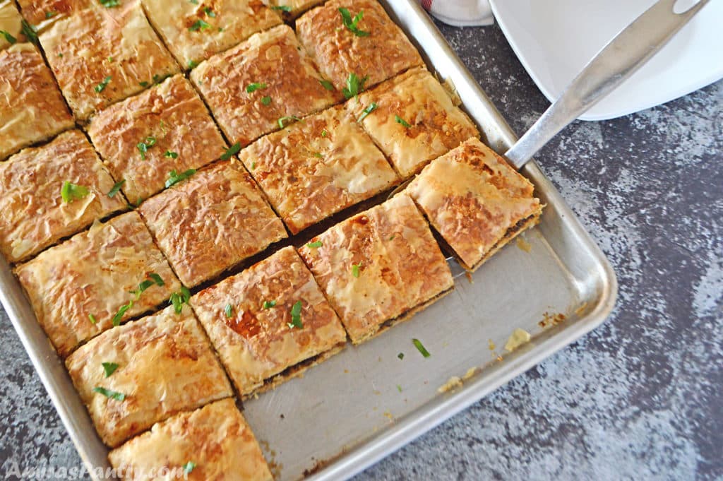 A baking sheet with phyllo squares cut side by side and placed on a dark grey table.