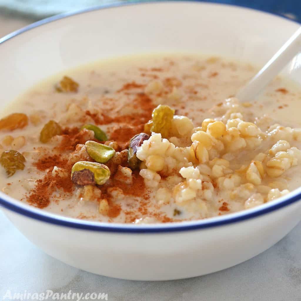 Cooked wheat berries in a white bowl with milk and garnished with cinnamon and pistachios.