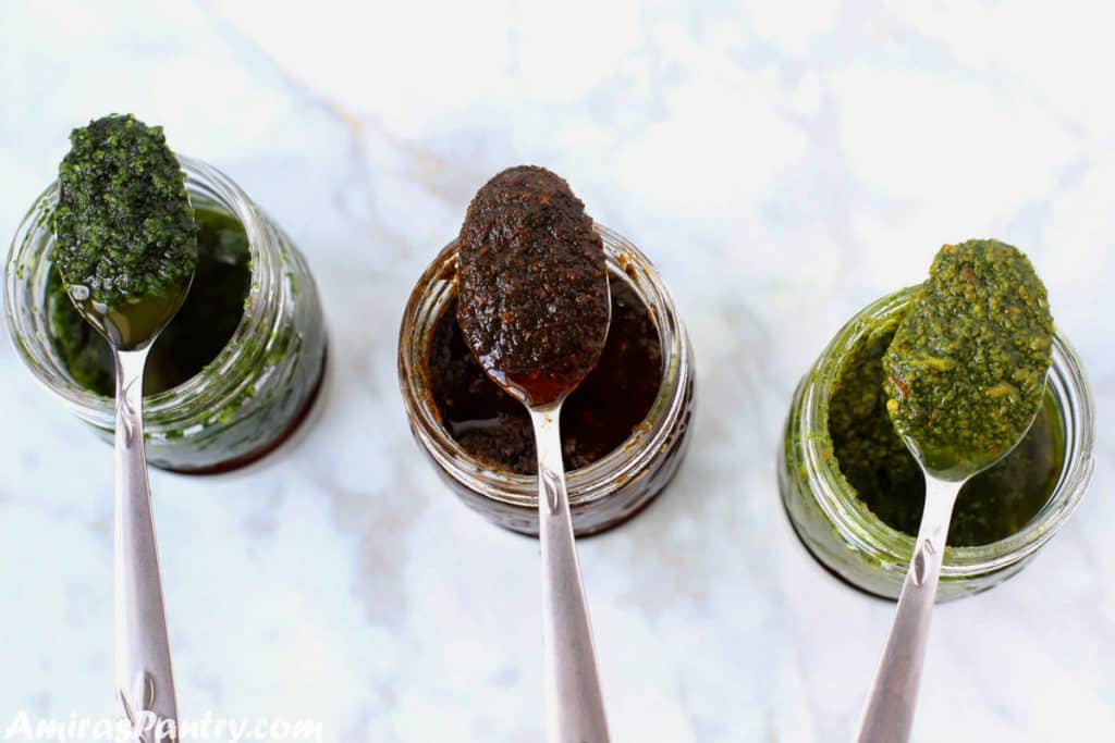 Three spoons filled with different Chermoula sauces and placed over the top of the corrisponding Chermoula jar.