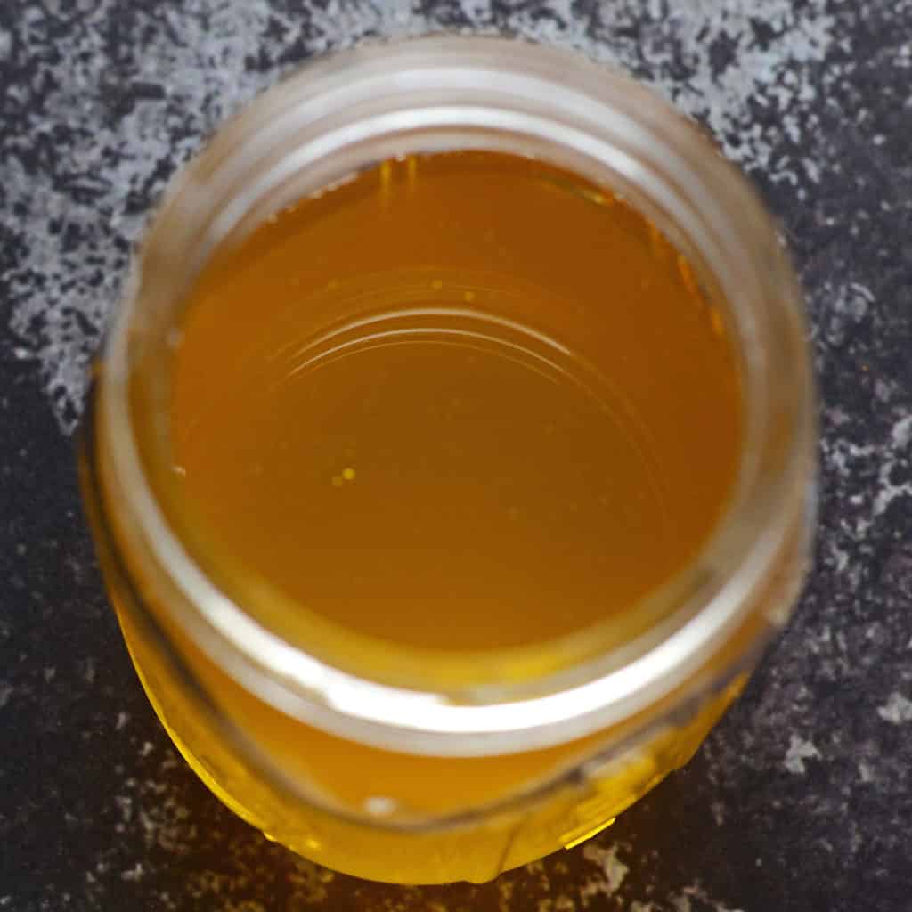 A mason jar filled with clear golden ghee on a black background