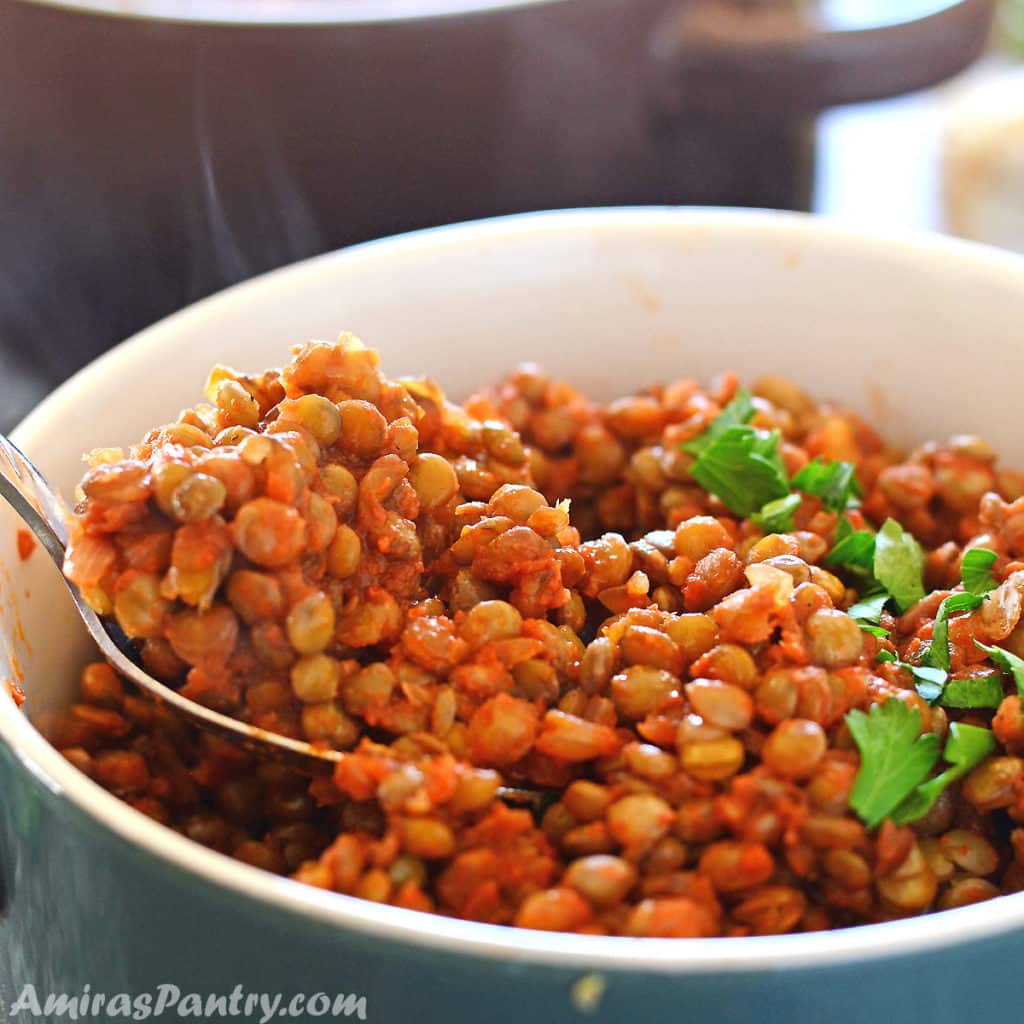 Lentil stew in a green bowl with a spoon scooping up some lentils.