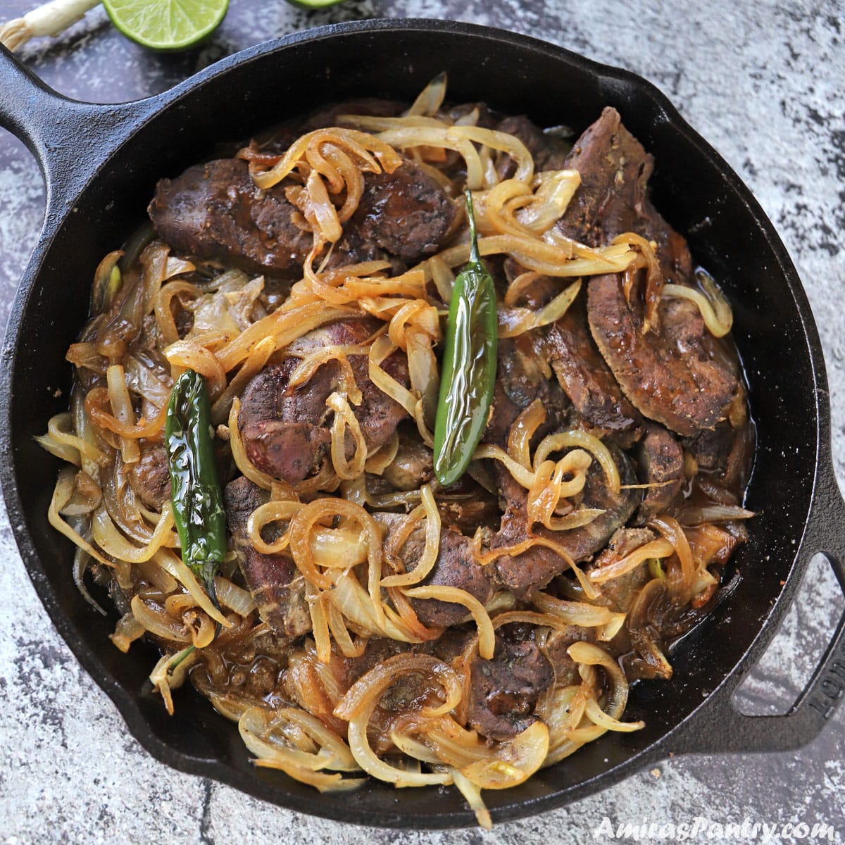 A cast iron skillet with beef liver and onions garnished with chili peppers on top.