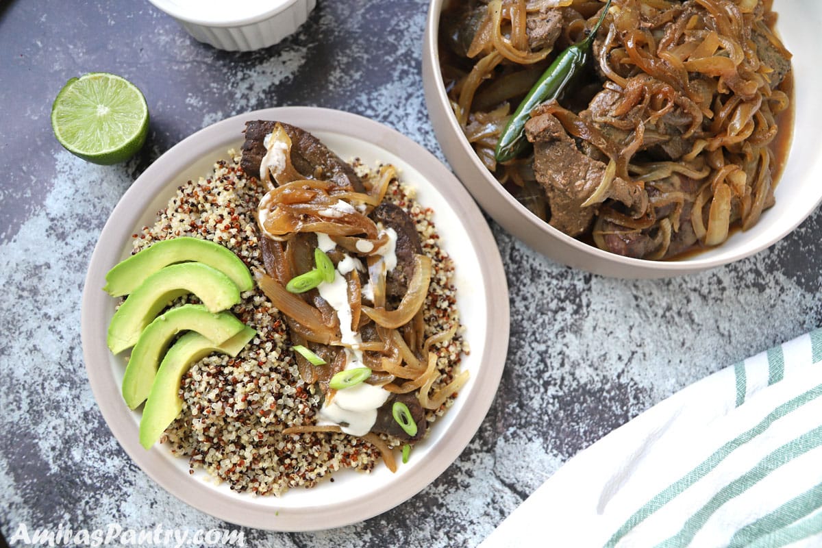 A plate with a serving of beef liver with some quinoa and sliced avocado on a concret table with half a lemon