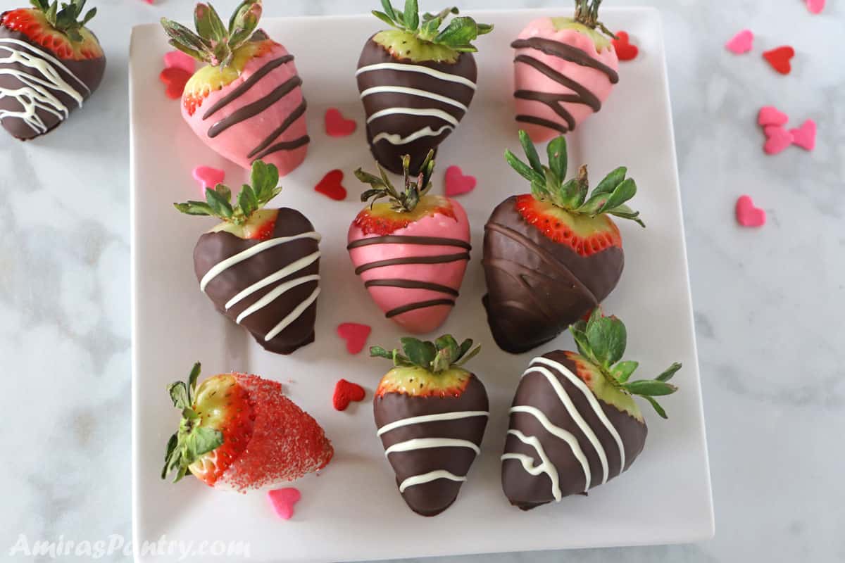 Chocolate covered strawberries in pink, white and brown colors with heart sprinkles on a white square plate
