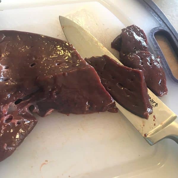 Liver placed on a cutting board with a knife  cutting pieces of it.