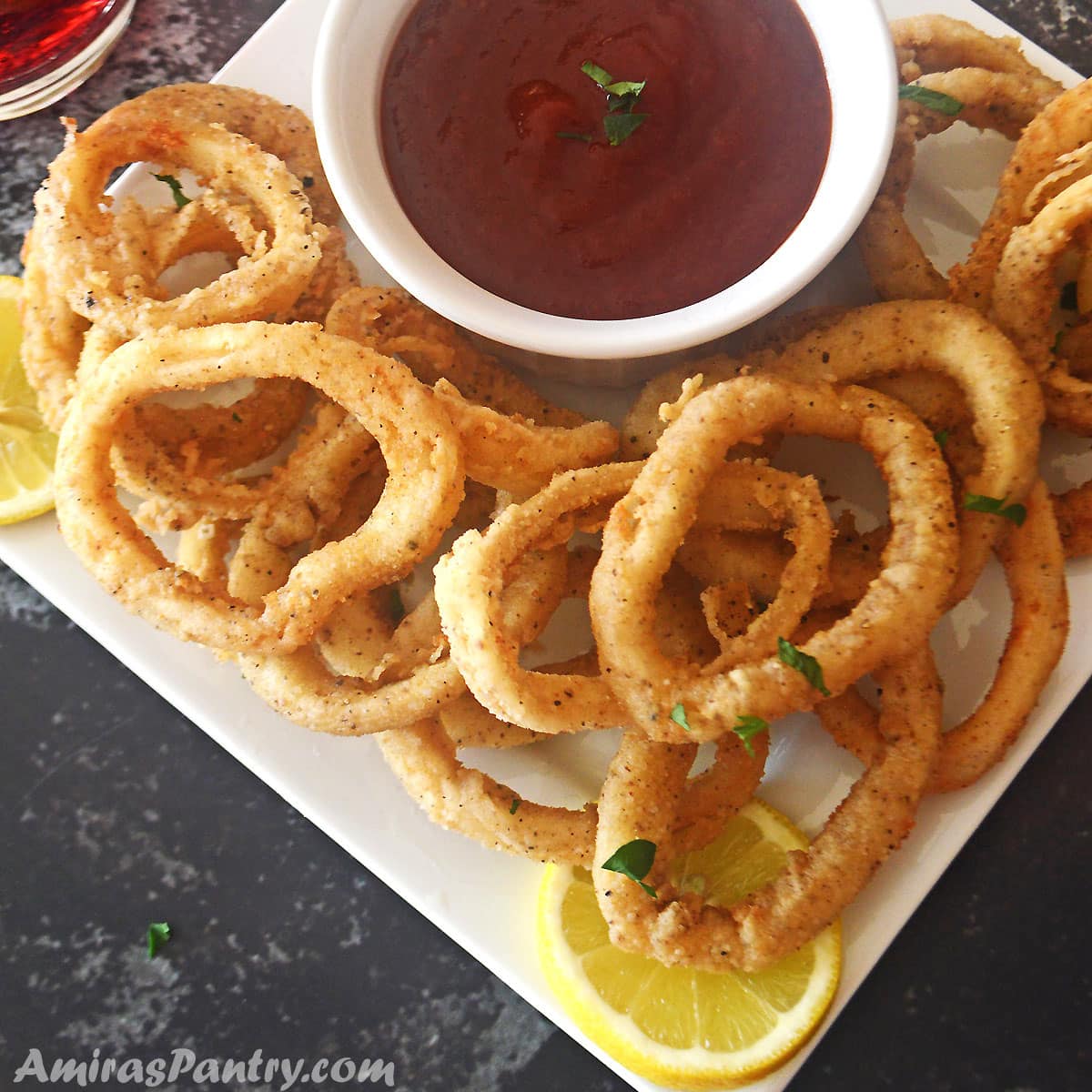 Fried calamari rings on a white serving plate with a bowl of sauce in the middle.