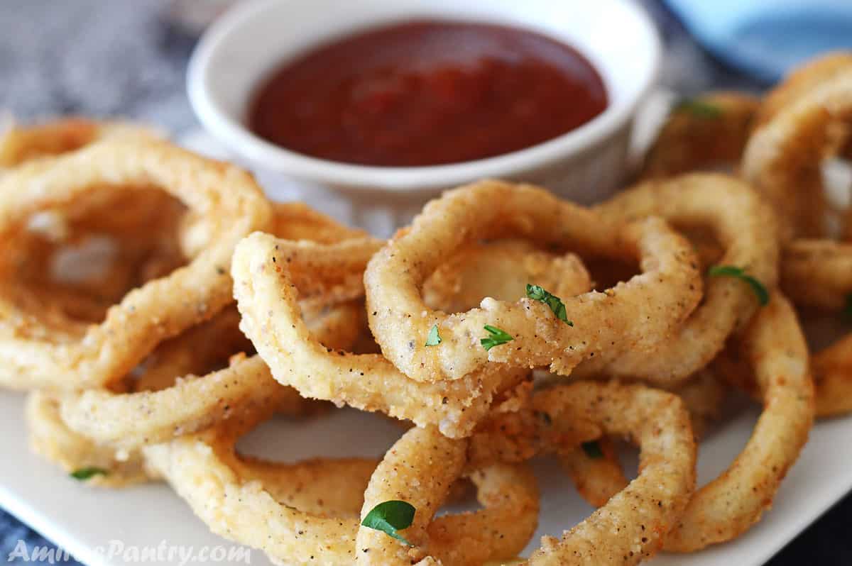 Fried calamari garnished with parsley on a white plate with a bowl of sauce in the back.