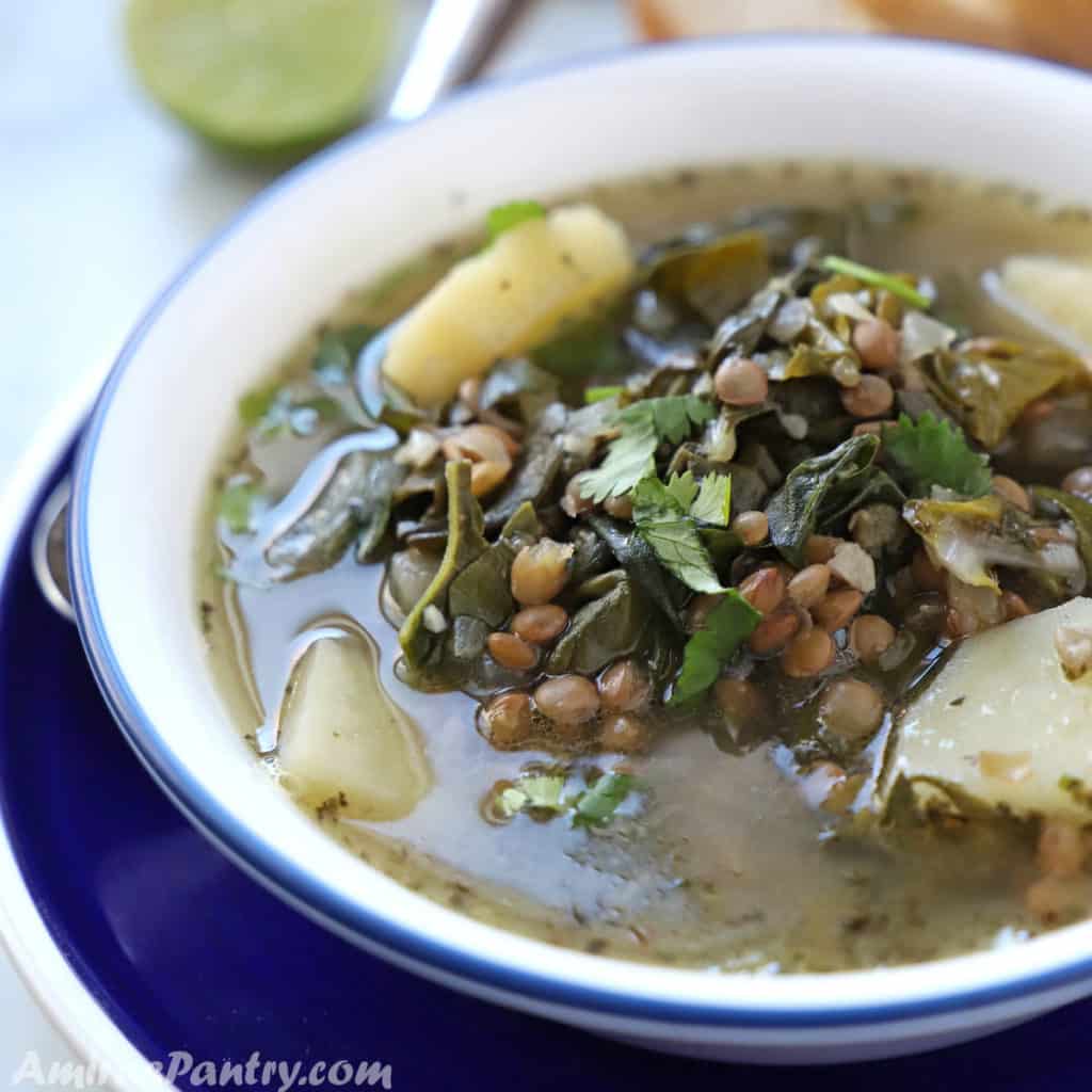 Lebanese brown lentil soup in a white plate with a blue rim placed on another blue dish with a spoon on the side.