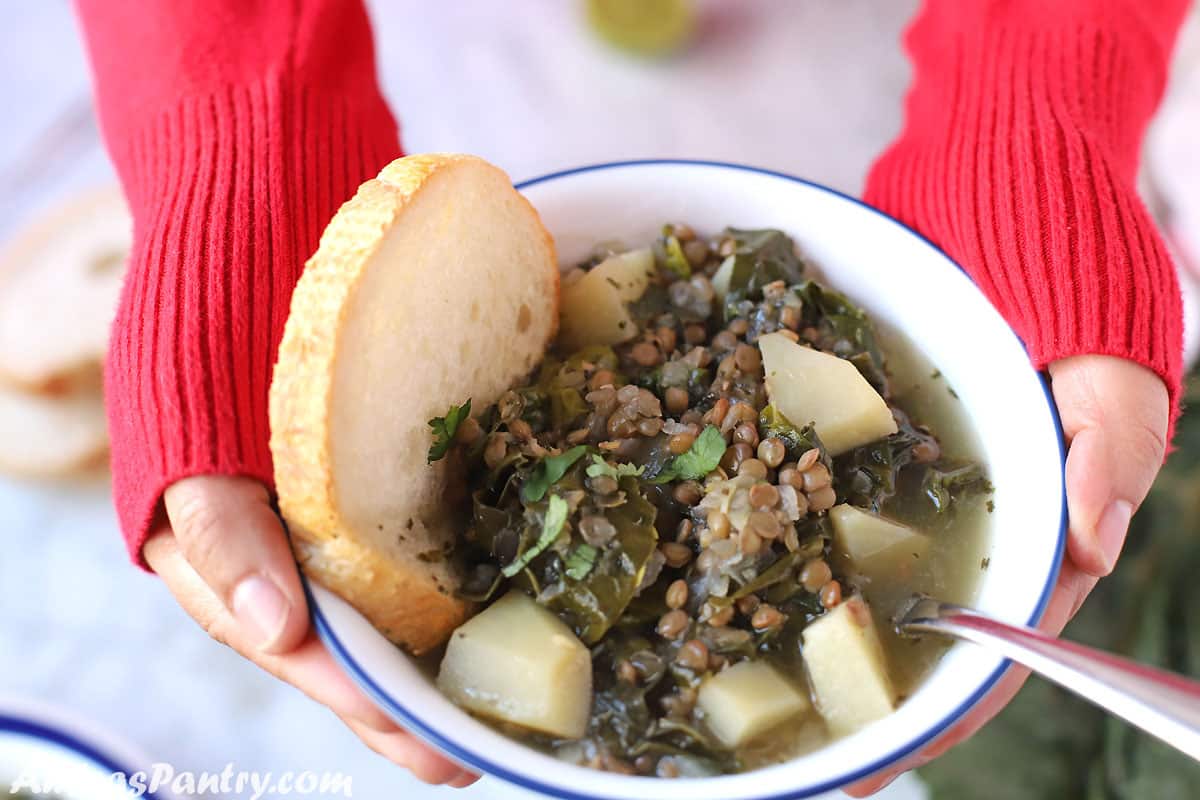 Hand holding a white bowl with Lebanese lentil soup with a piece of crusty bread.