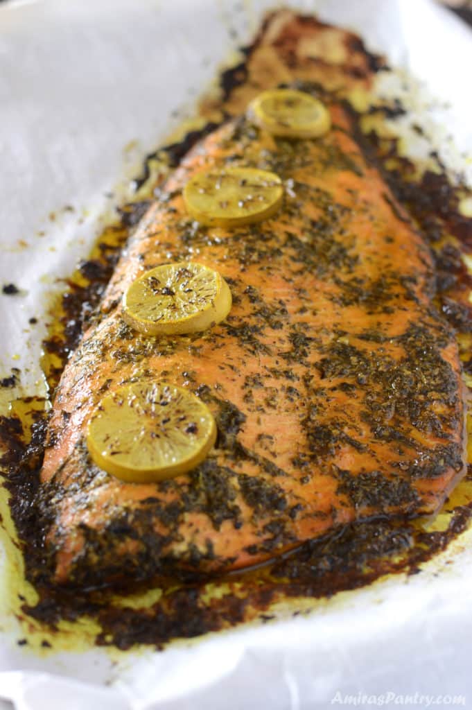 A wholw salmon fish placed on a baking sheet and garnished with lemon rings