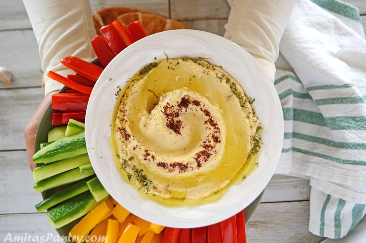 hands holding a serving platter of hummus and veggies.