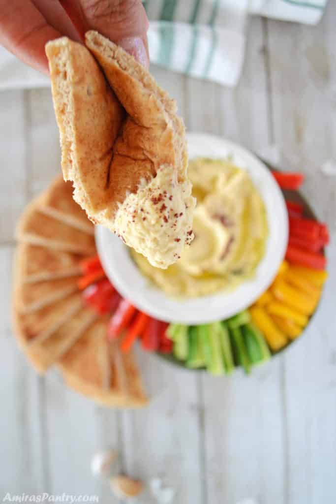 Hand holding a piece of pita bread dipped in hummus.