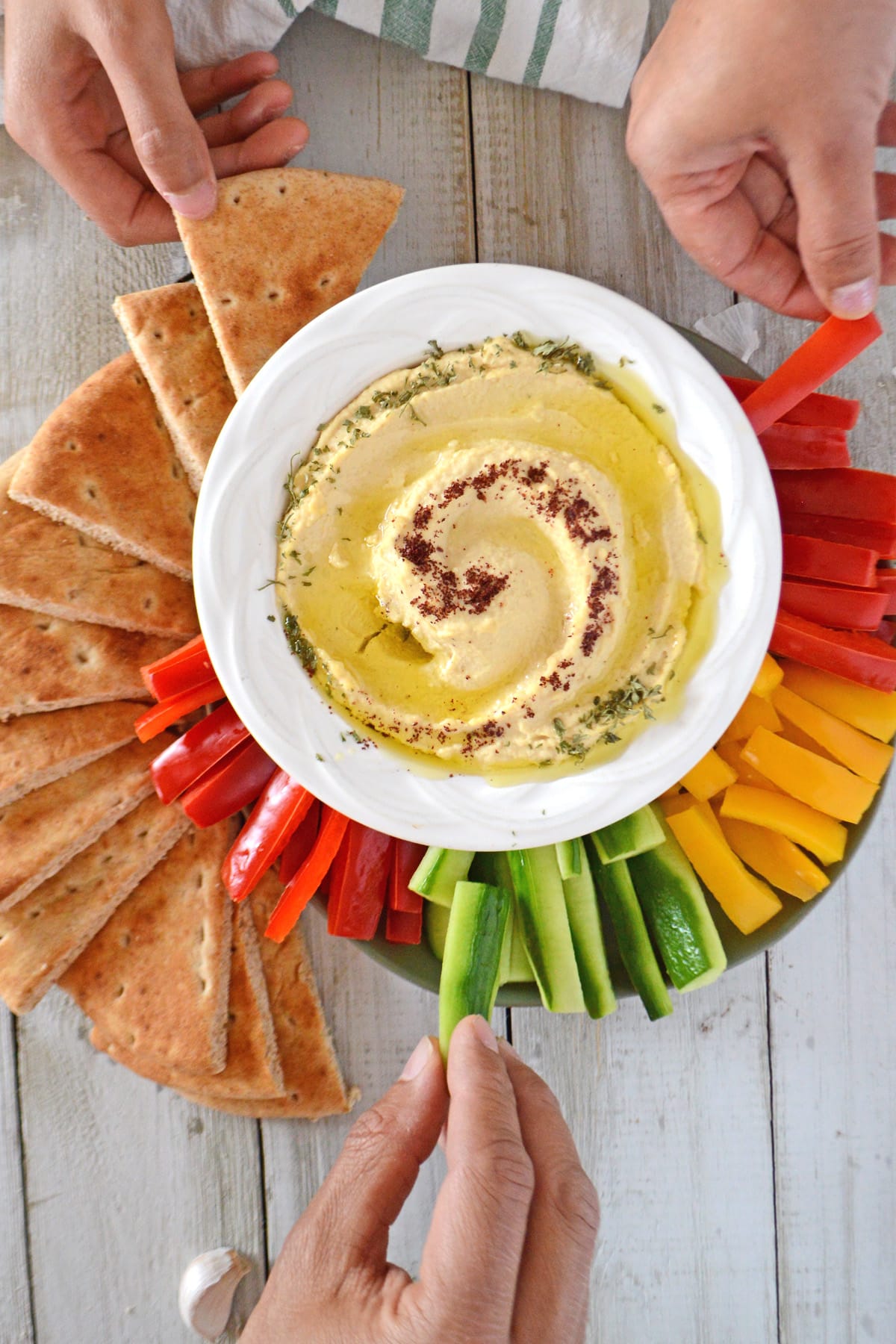 hands reaching out for veggie strips and pita wedges with a big bowl of hummus on the center.