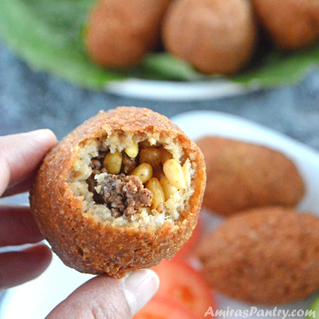 A hand holding one kibbeh open from one side showing the ground beef filling with pine nuts.