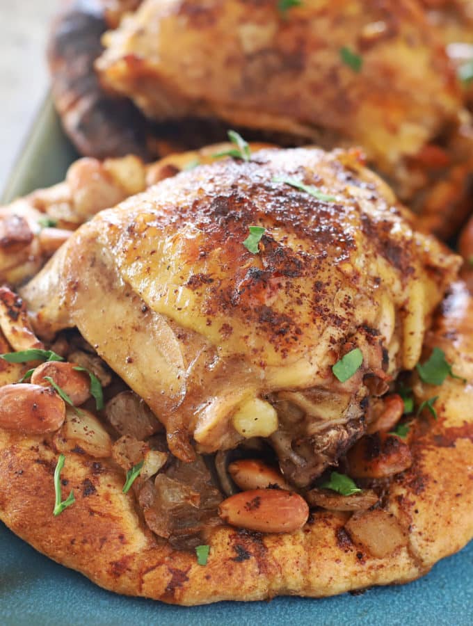 roasted sumac chicken on musakhan bread with almonds and onions on a blue serving platter.