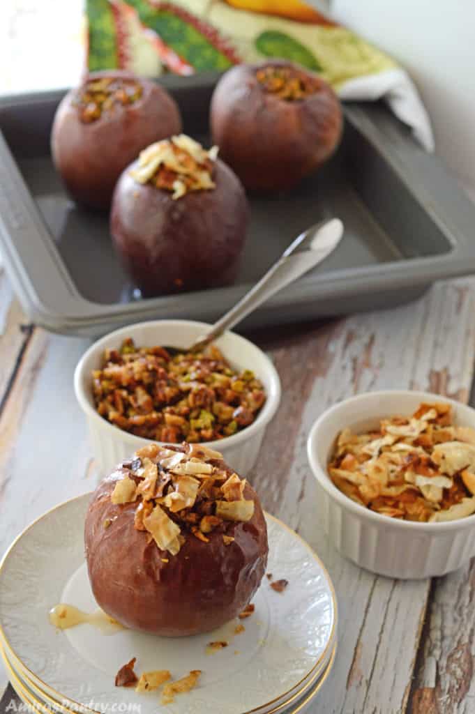 Baked apples on a wooden table with some bowls with nuts and baked phyllo dough.