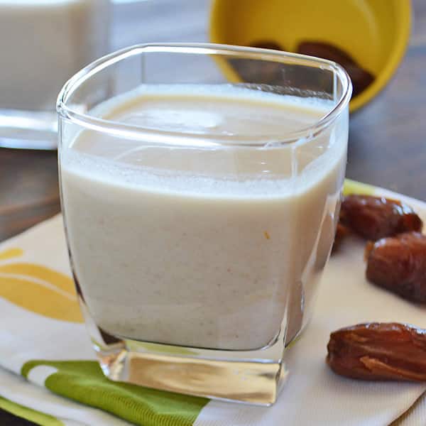 A cup of date milkshake on a white and yellow napkin on a wooden table with some dates on the side.