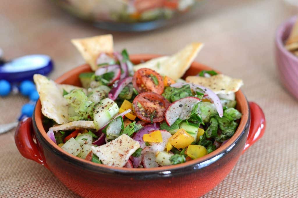 A small red bowl of salad placed on a burlap surface.