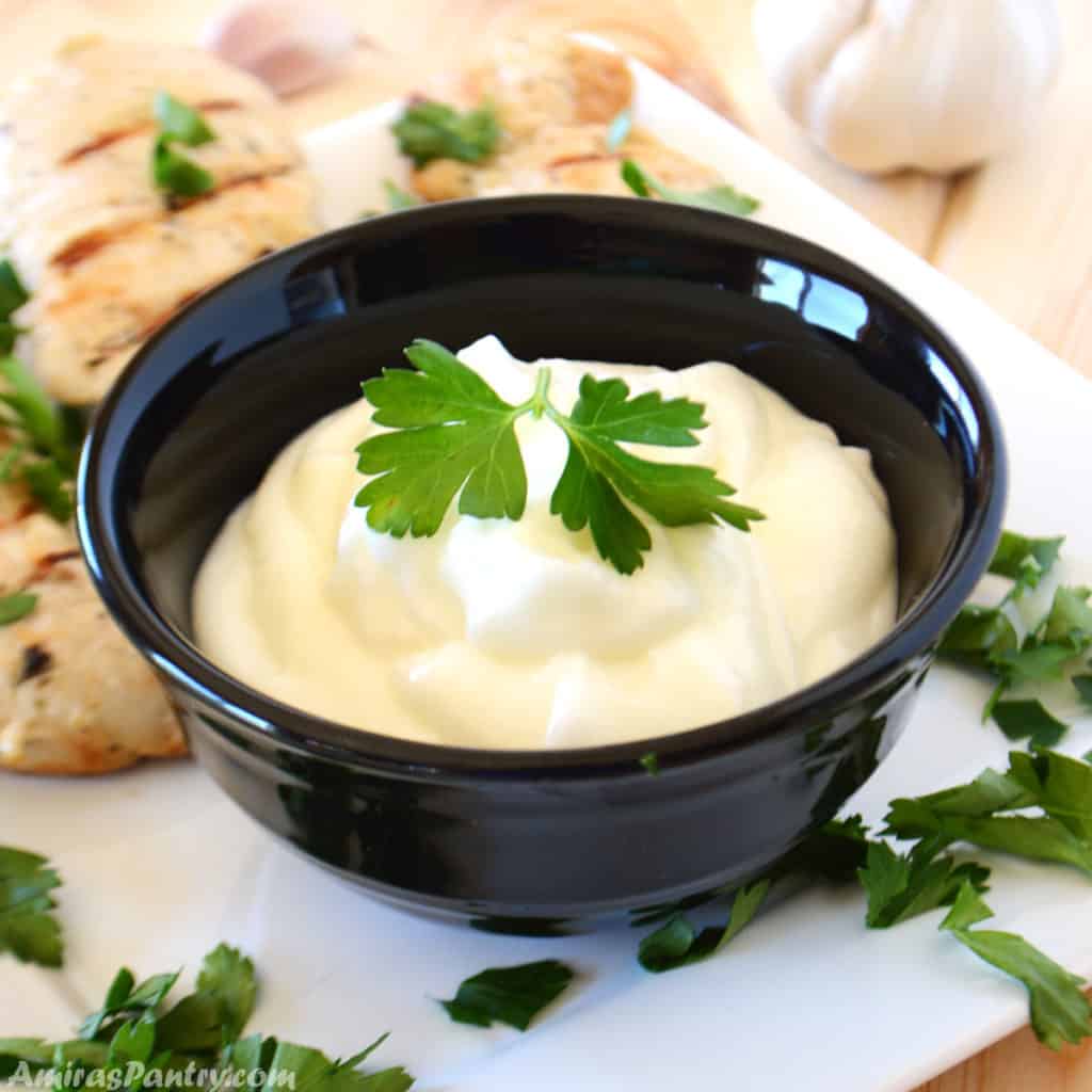 Garlic dip in a small black bowl garnished with parsley