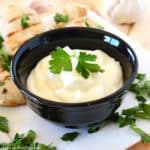 Garlic dip in a small black bowl garnished with parsley