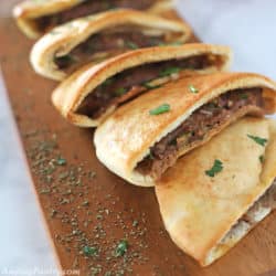 An array of hawawshi halves on a wooden serving board garnished with parsley