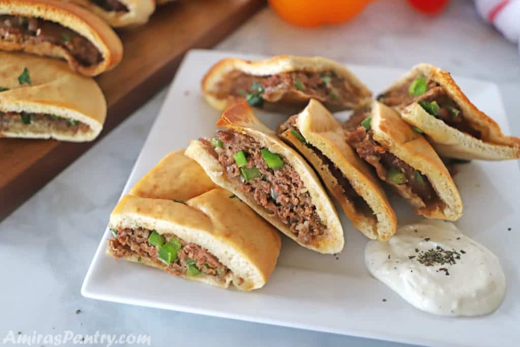 Hawawshi pitas cut into quarters and placed ona white serving plate with a dollop of tzatziki next to it.