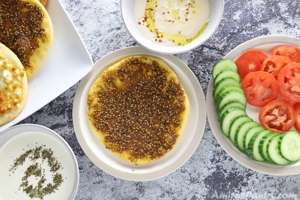 Breakfast table with middle eastern pizza along with sauces and a plate of diced tomato and cucumber.