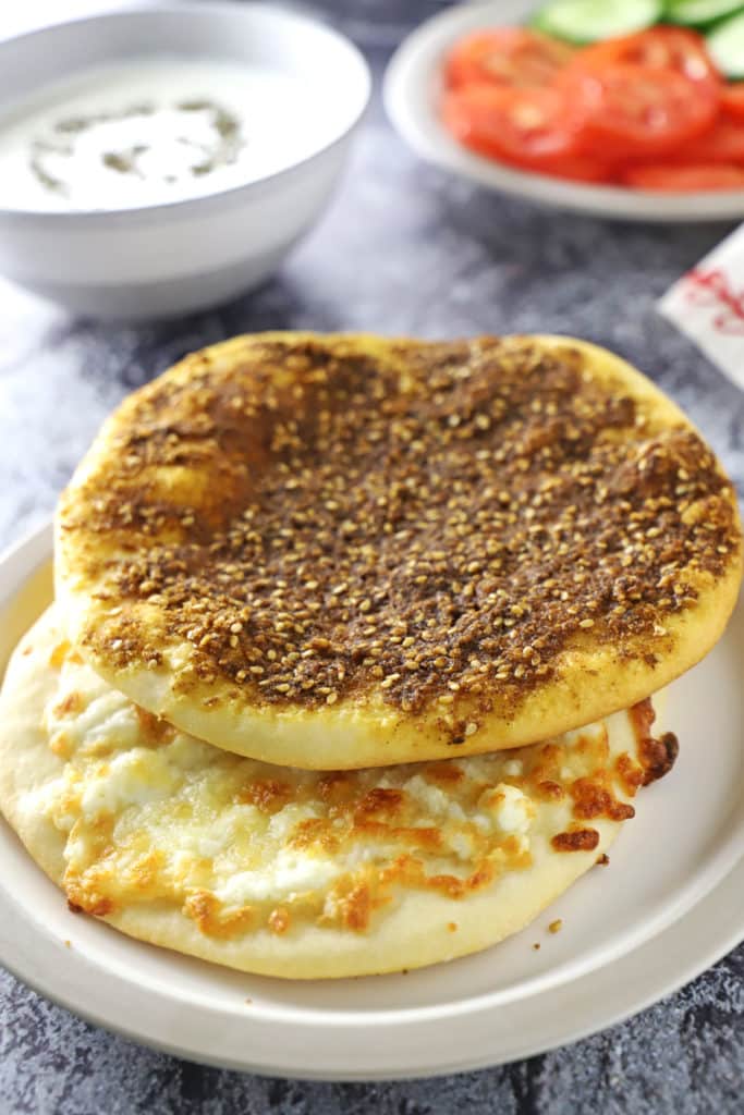 Za'atar and cheese manakish placed on a concret surface with bowls of dips in the back.