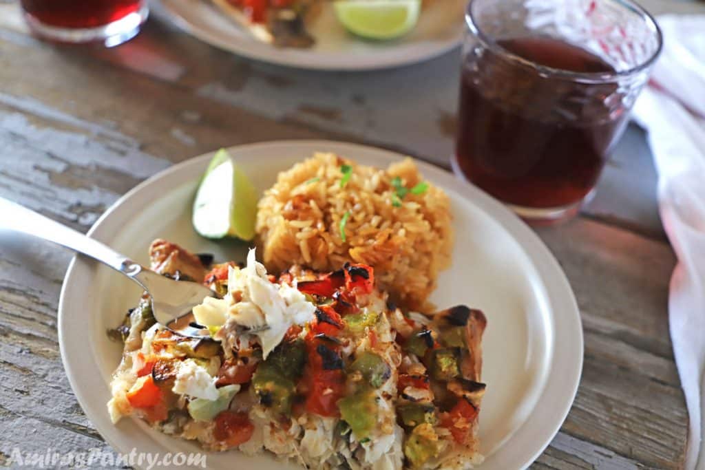 A plate with rice and a piece of baked bass with a fork and a cup of juice on the side.