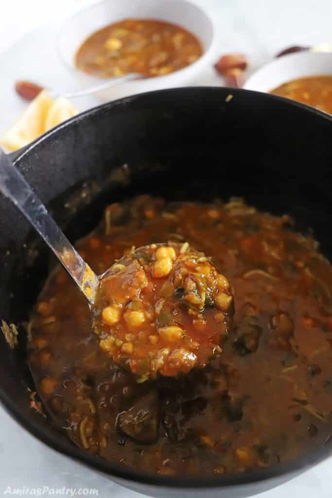 A ladle scooping some soup out of a cast iron pot.