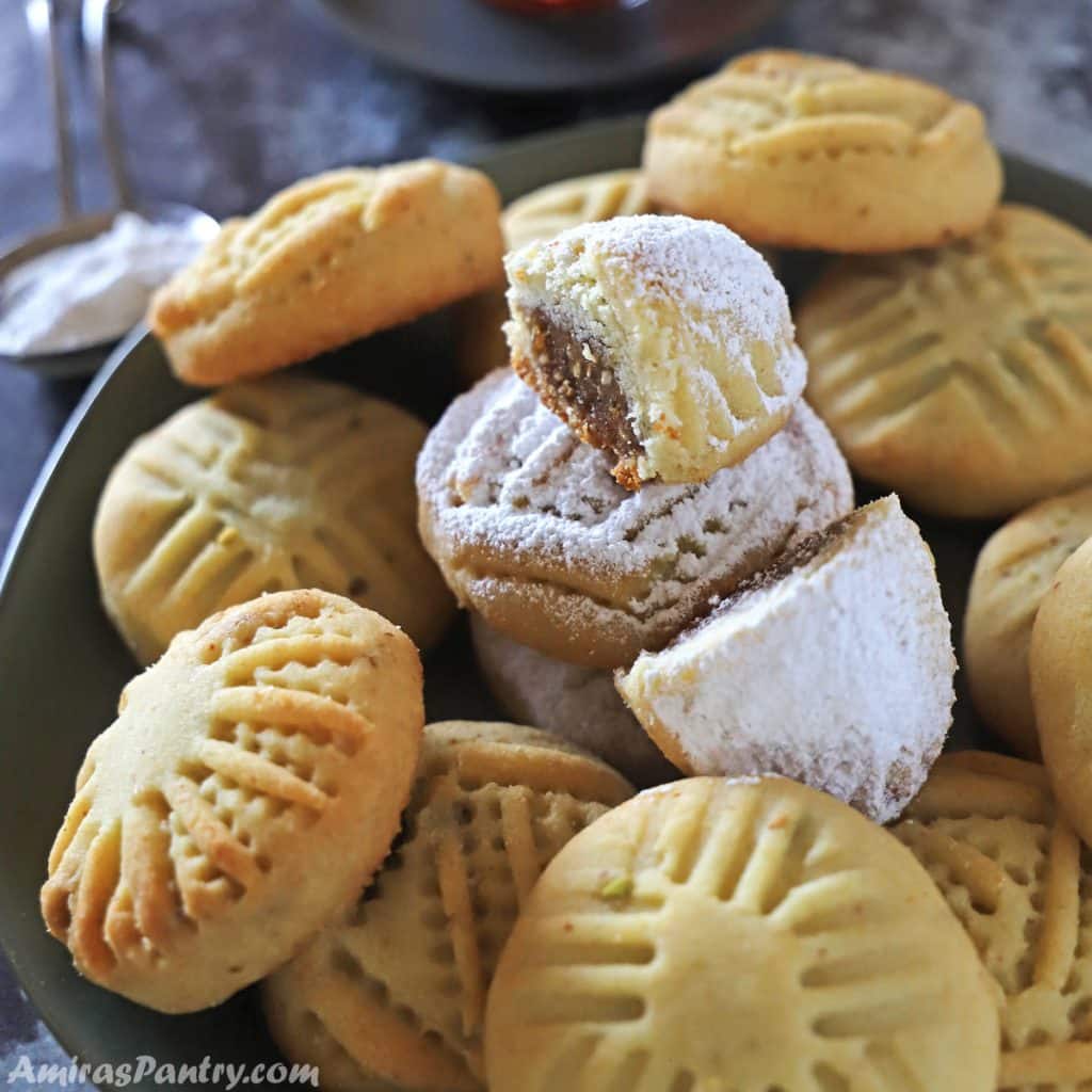 cookies on a black metal serving plate with one maamoul on the top and cut in half to show date filling.