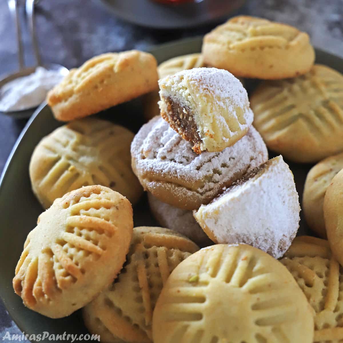 cookies on a black metal serving plate with one maamoul on the top and cut in half to show date filling.