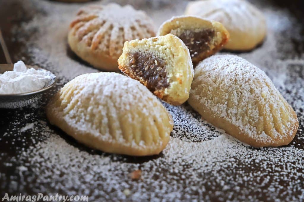 sugar dusted cookies on a baking sheets with one cut in halves showing date filling.