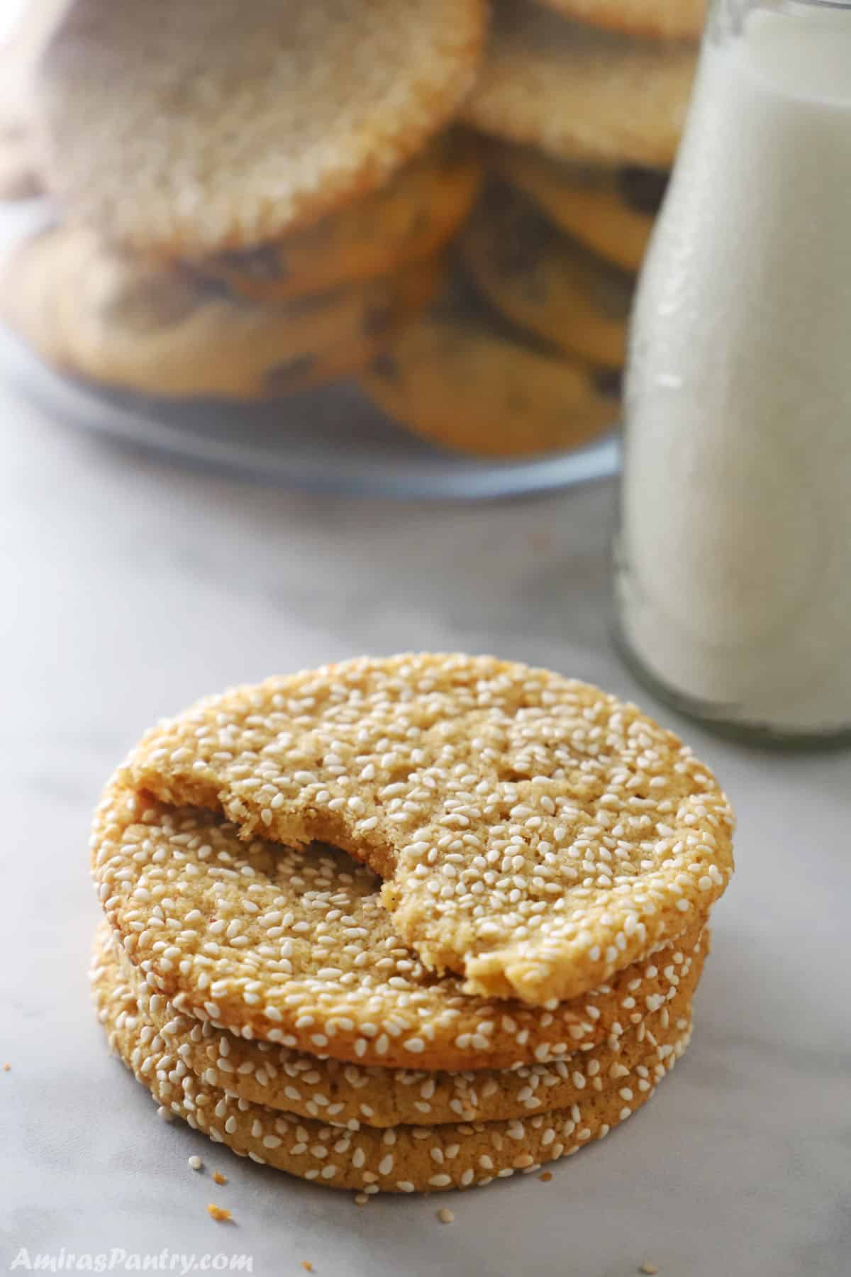 A stack of tahini cookies with a bottle of milk in the back.