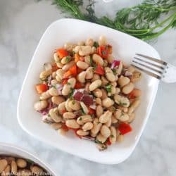 white plate with bean salad and a dill weed on the side.