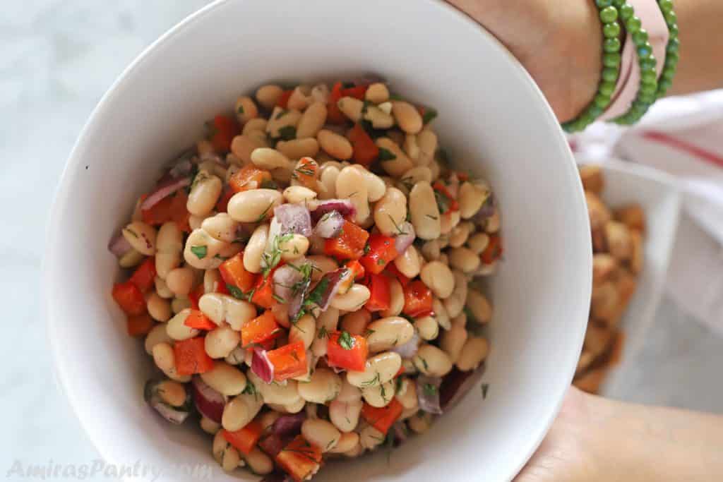 Hands holding a serving white plate of bean salad