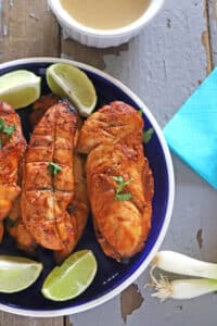 grilled chicken tenders on a blue plate placed on a wooden table with green onions on the side.