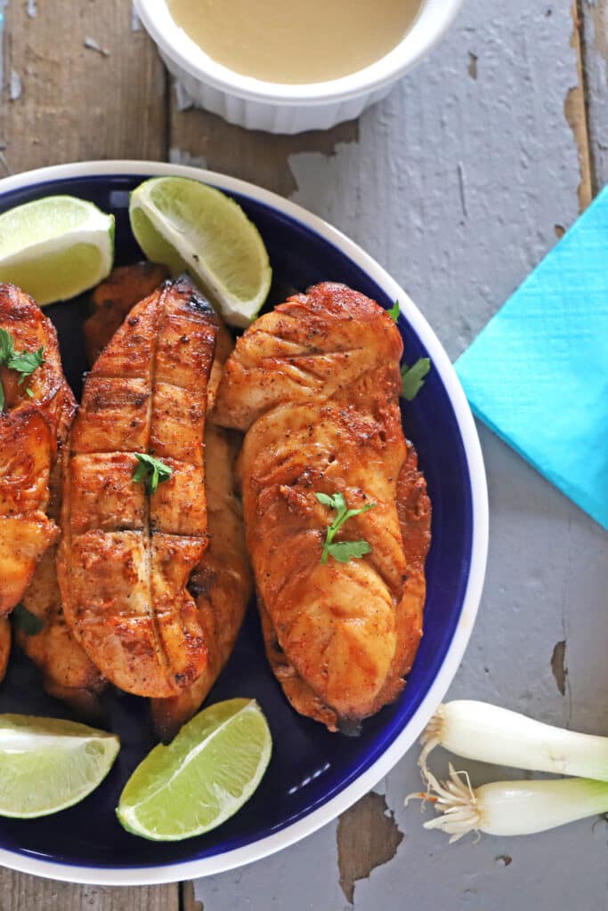 grilled chicken tenders on a blue plate placed on a wooden table with green onions on the side.