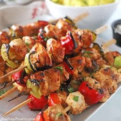 Tawooq skewers on a white plate with a bowl of yellow rice on the back.