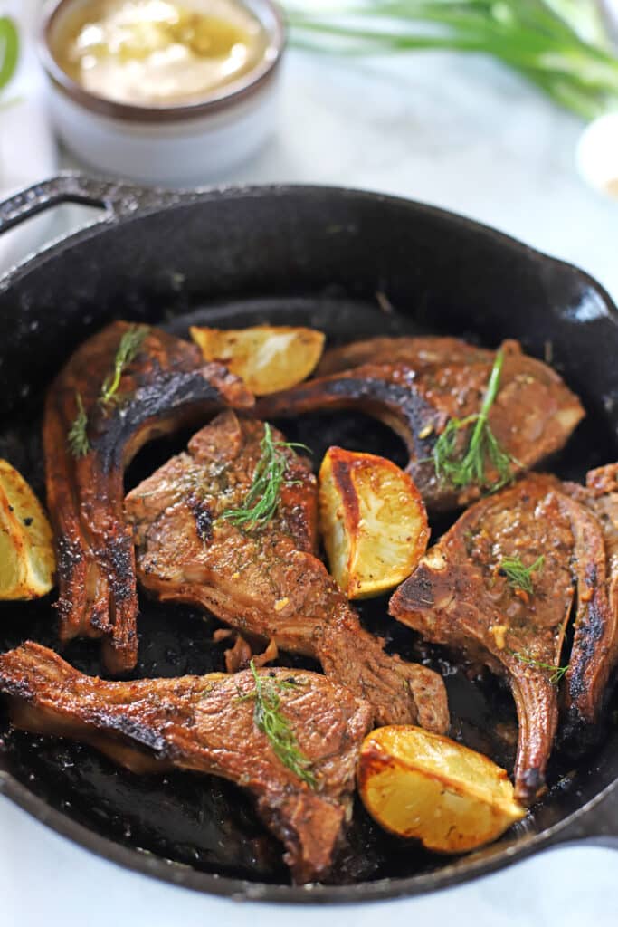 lamb chops on a cast iron skillet with lemon wedges on the side.