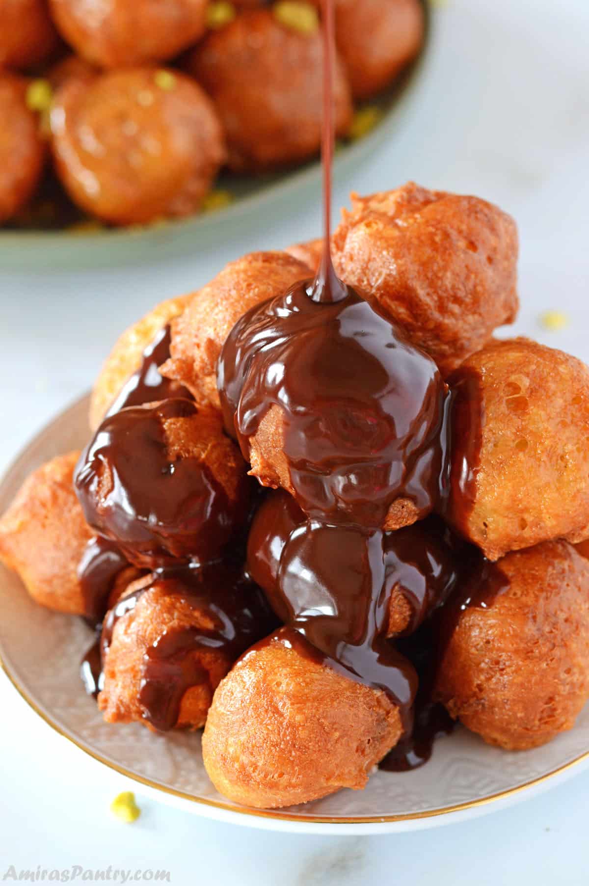 Chocolate ribbons being poured over a white plate of loukoumades.