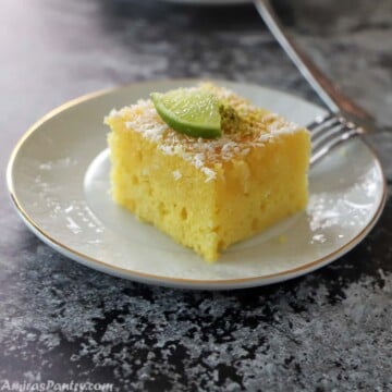 A piece of Revani cake on a white plate placed on a black tabletop.