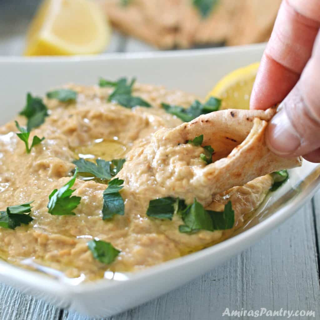 A hand scooping some baba ganoush with a piece of pita bread.