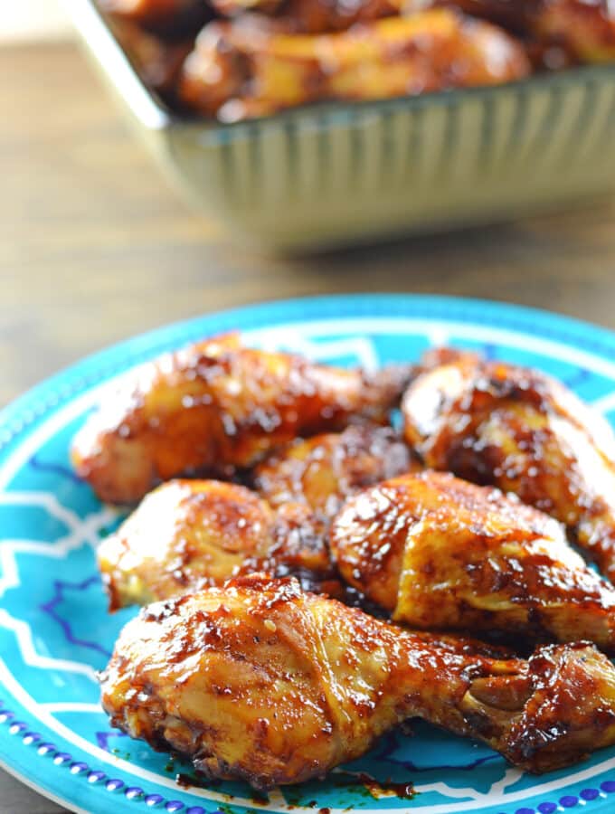 BBQ drumsticks on a light blue plate with another big grey bowl in the back full of drumsticks